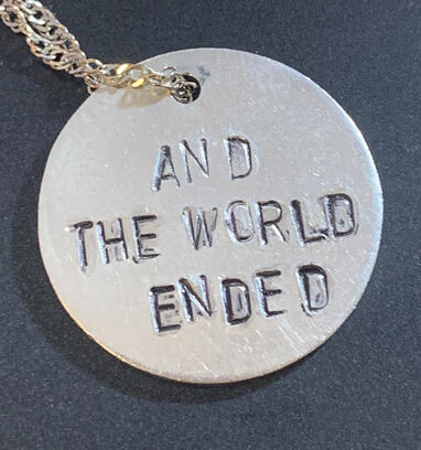 a circular silver pendant on a necklace, featuring the text "ride or die", the text is inked in red